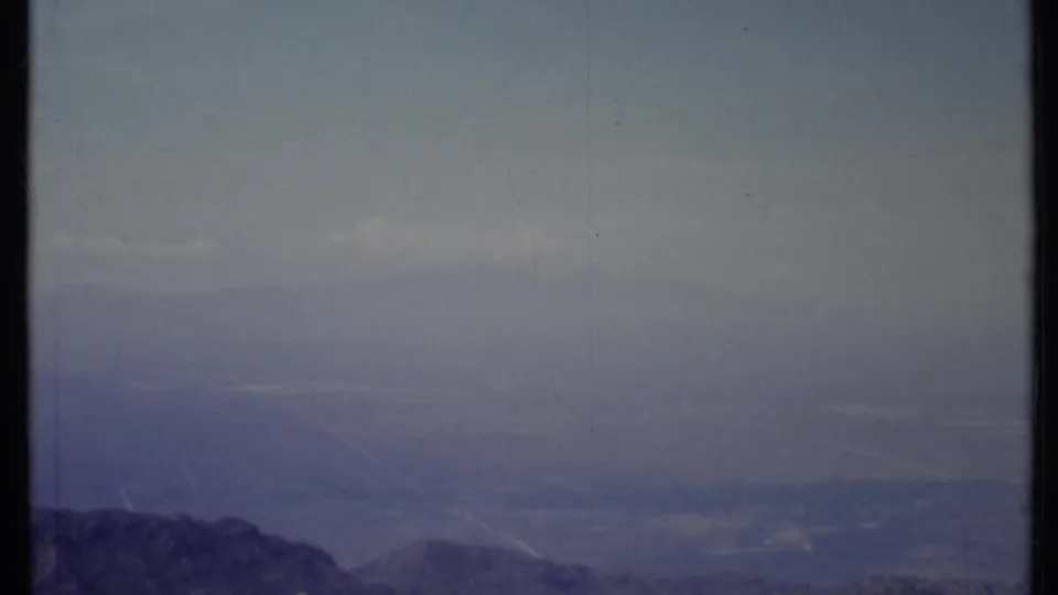 1971 California 8mm landscape view with a low dark ridgeline, distant valley floor, and muted haze across the horizon.