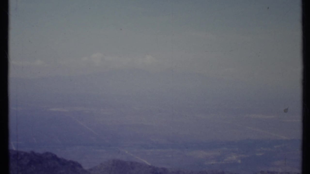 Hazy mountain ridge beneath a muted blue-purple sky with film scratches and border lines.