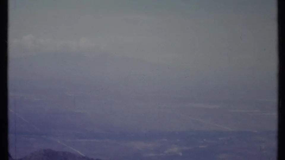 1971 California landscape frame with a hazy mountain horizon, pale cloud streaks, and muted archival color.