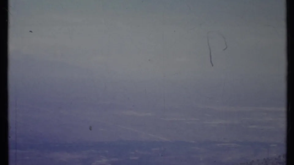 1971 California 8mm frame with a fog-softened sky, faint landscape below, scratches, and washed blue tones.