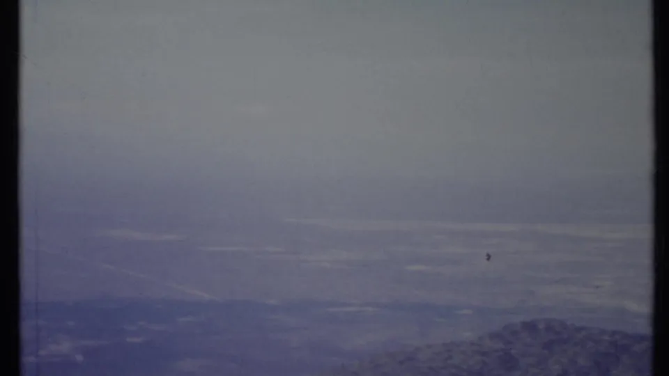 1971 California landscape frame showing a hazy valley, distant mountain edge, and pale cloud bands in archival 8mm color.