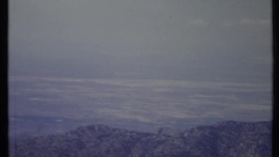1971 California 8mm frame with a dark foreground ridgeline, broad hazy valley, and soft blue-gray sky.