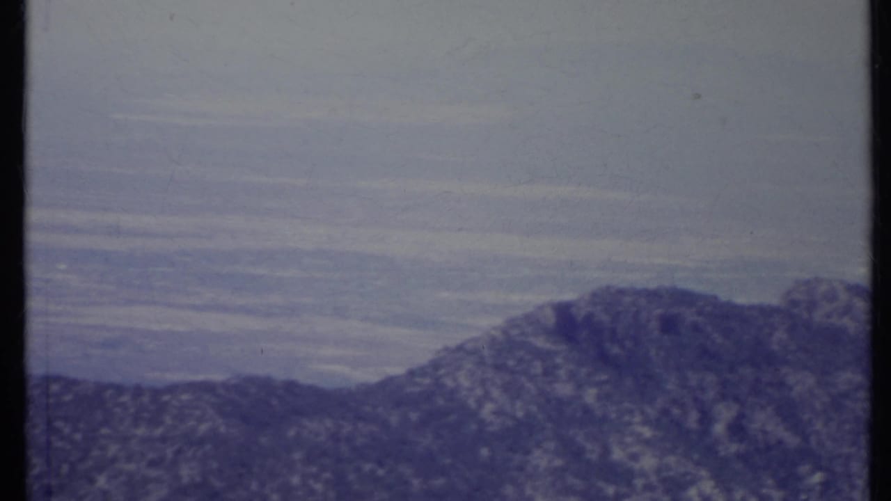 Rocky mountain ridge below a hazy sky with film frame edges visible.