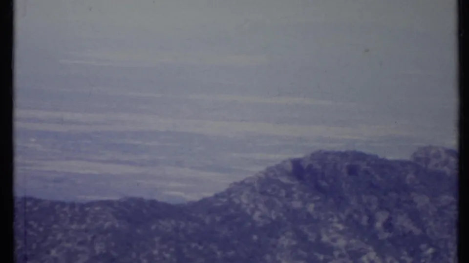 1971 California 8mm frame showing a rocky mountain ridge rising above a hazy valley and pale sky.