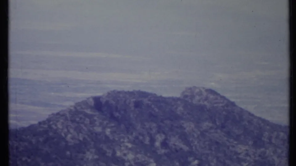 1971 California home-movie frame with a rugged mountain ridge and distant valley haze behind it.
