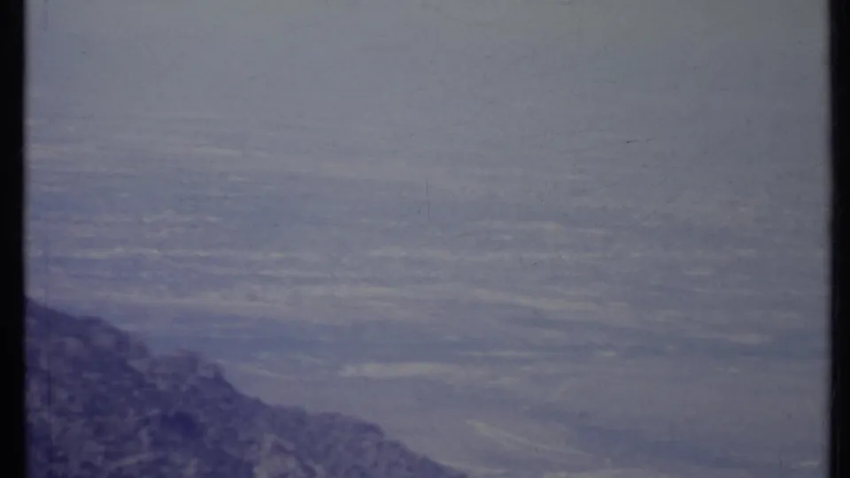 1971 California home-movie frame looking past a dark mountain ridge toward a distant hazy valley.