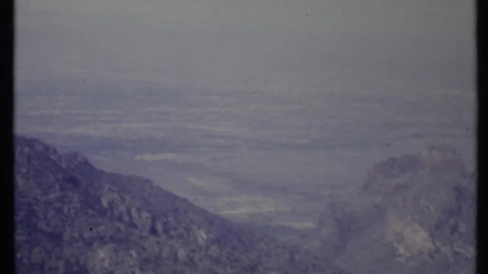 1971 California home-movie frame with a rugged ridge in the foreground and a hazy valley stretching into the distance.