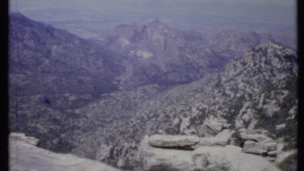 Hazy mountain range with pale rocky foreground and sparse trees.