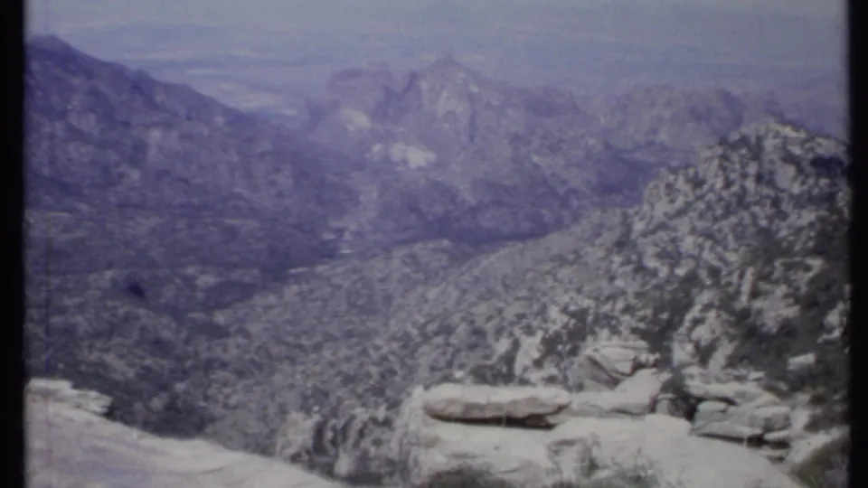 1971 California 8mm frame showing layered mountains, a rocky overlook, and sparse vegetation under a hazy sky.
