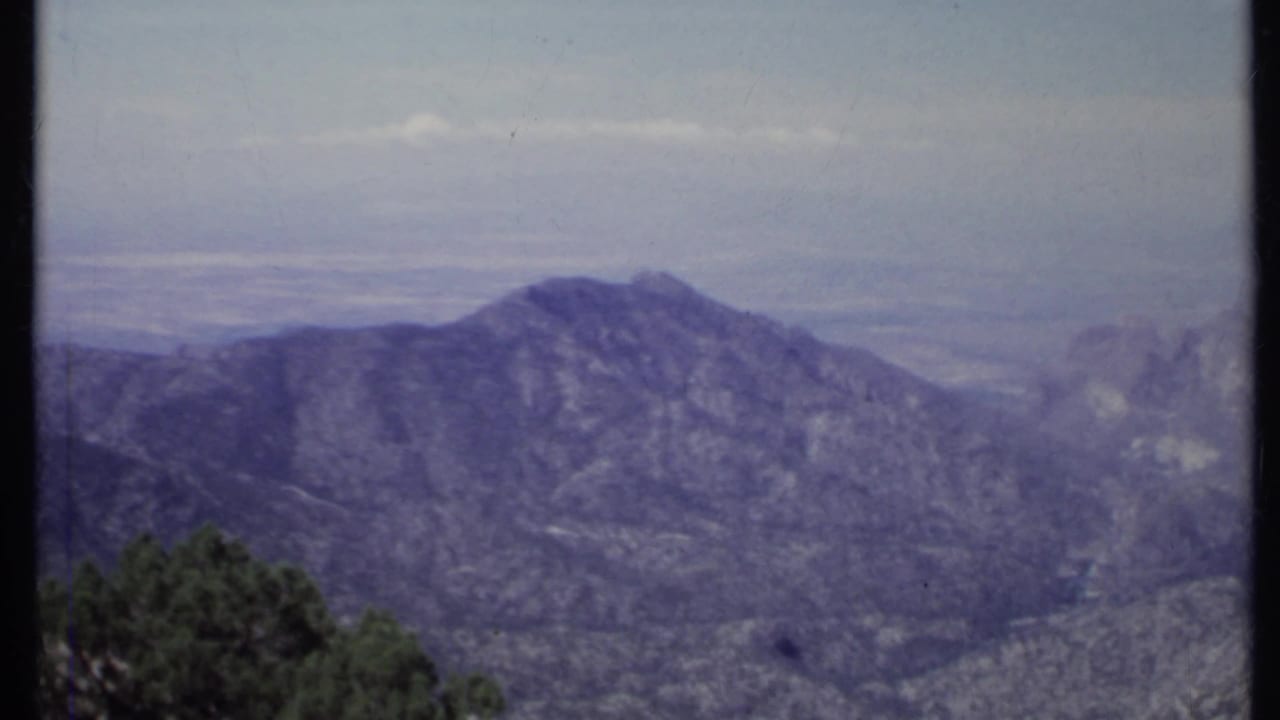 Hazy mountain ridge above a distant valley with dark trees along the lower edge.