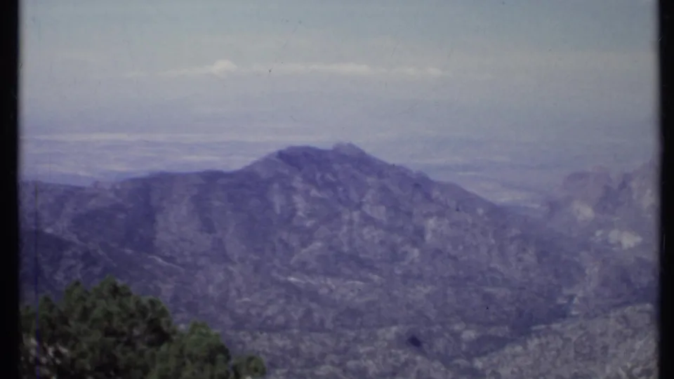 1971 California 8mm frame showing a high view across a rugged mountain ridge, pale sky, and hazy valley beyond.