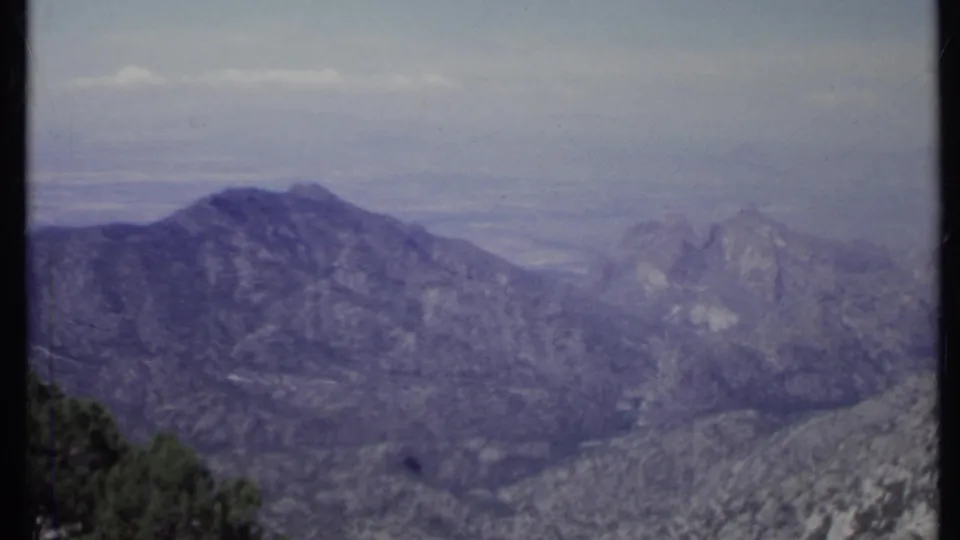 1971 California 8mm frame with hazy layered mountain slopes and dark green trees along the foreground.
