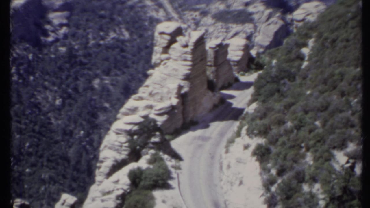 Narrow dirt road cut through pale rock on a steep mountain slope.