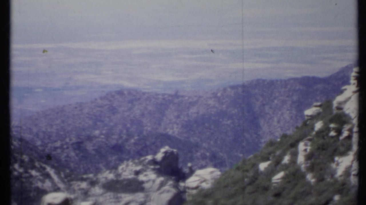 Rocky mountain slope with forested ridges and a hazy valley beyond.