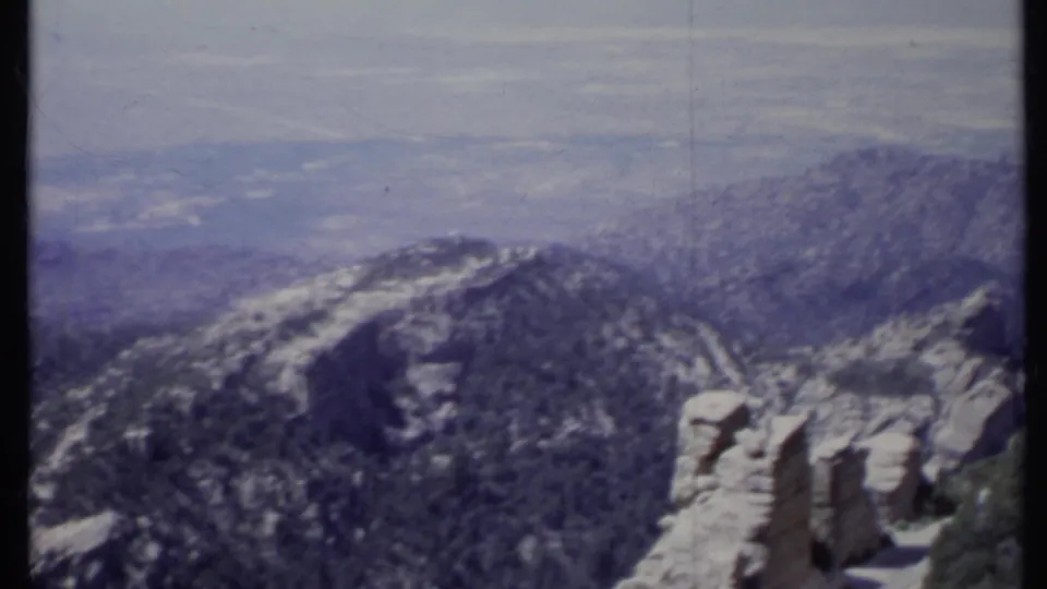 1971 California 8mm frame looking across a tree-covered ridge, light rock faces, and a broad valley softened by haze.