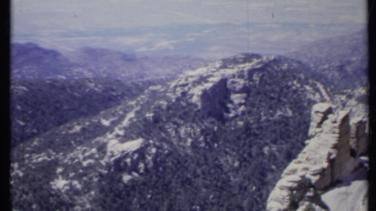 Forested mountain ridge with pale rock outcrops and distant hazy terrain.