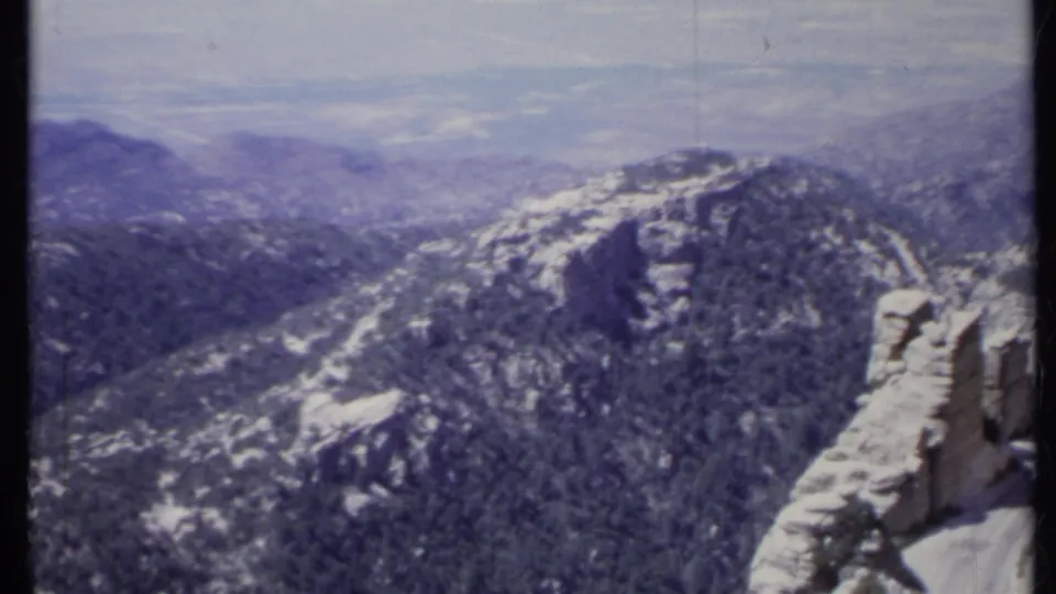 1971 California 8mm frame showing a high view over forested mountain ridges and pale rock formations in hazy distance.