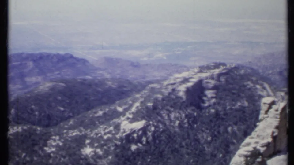1971 California 8mm frame of rugged mountain terrain, distant haze, and a pale rock edge along the right side of the view.