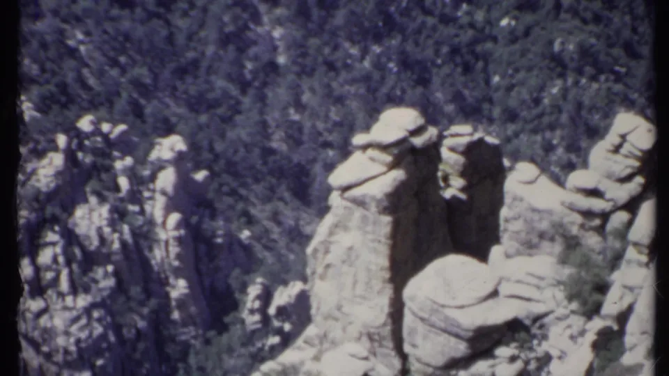 1971 California 8mm frame showing clustered pale rock spires and wooded mountain slopes below a hazy ridge line.
