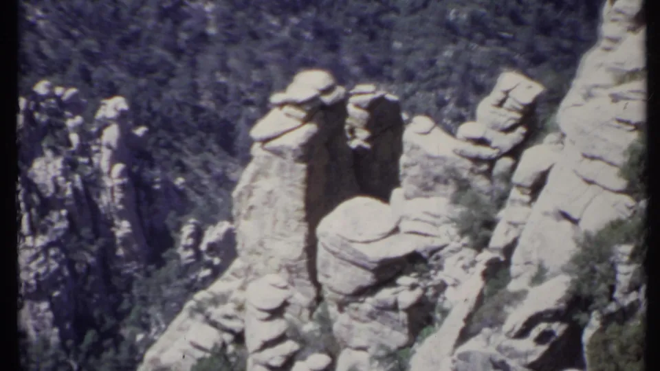 1971 California 8mm frame with a closer view of pale, stacked rock formations overlooking dense wooded mountain terrain.