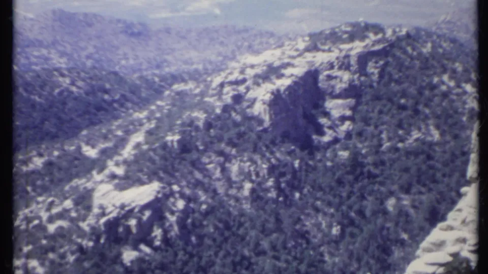 1971 California 8mm frame presenting a wide view of pine-covered ridges, pale rock formations, and a deep valley.