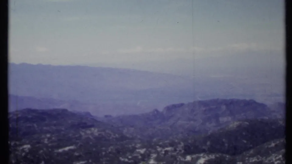 1971 California 8mm frame showing blue-gray mountain layers, a hazy sky, and darker forested slopes in the foreground.