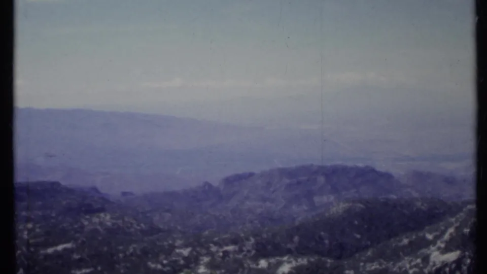 1971 California 8mm frame showing layered mountain ridges, rocky terrain, and a hazy pale sky from a high vantage point.