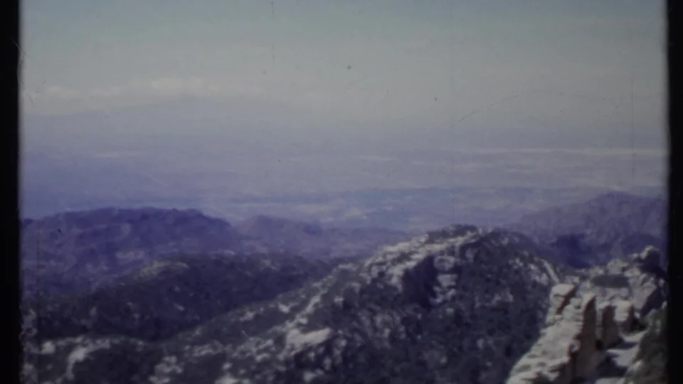 1971 California 8mm frame of a mountain panorama, with rocky foreground forms and a soft hazy valley beyond.