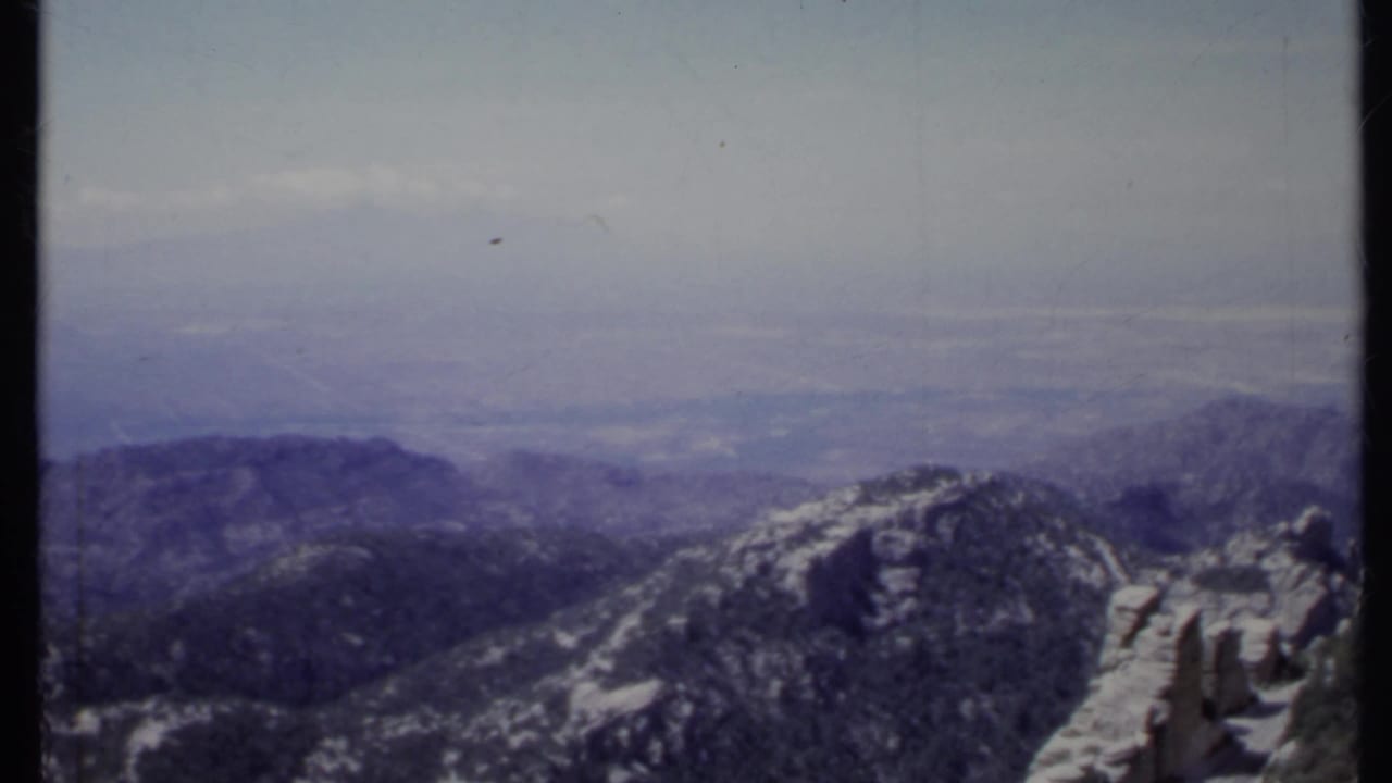 Snow-dusted rocky mountain ridge beneath a hazy cloudy sky.