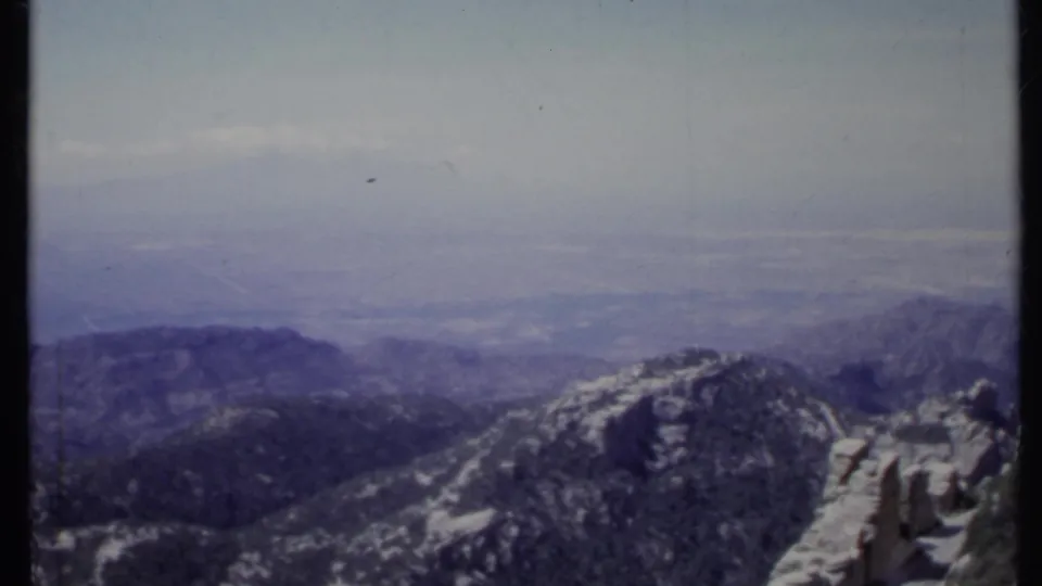 1971 California 8mm view of a rocky, snow-dusted mountain ridge fading into a cloudy horizon.