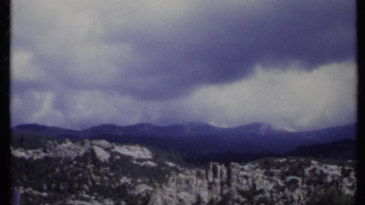 California mountain range in 1971 home-movie footage, with snow patches and heavy clouds over distant ridges.