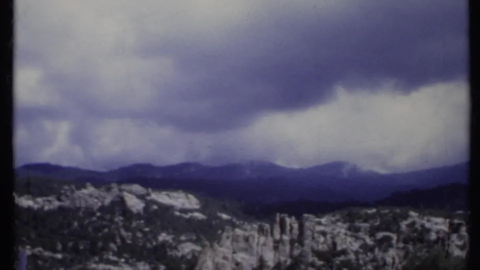 California mountain range in 1971 home-movie footage, with snow patches and heavy clouds over distant ridges.