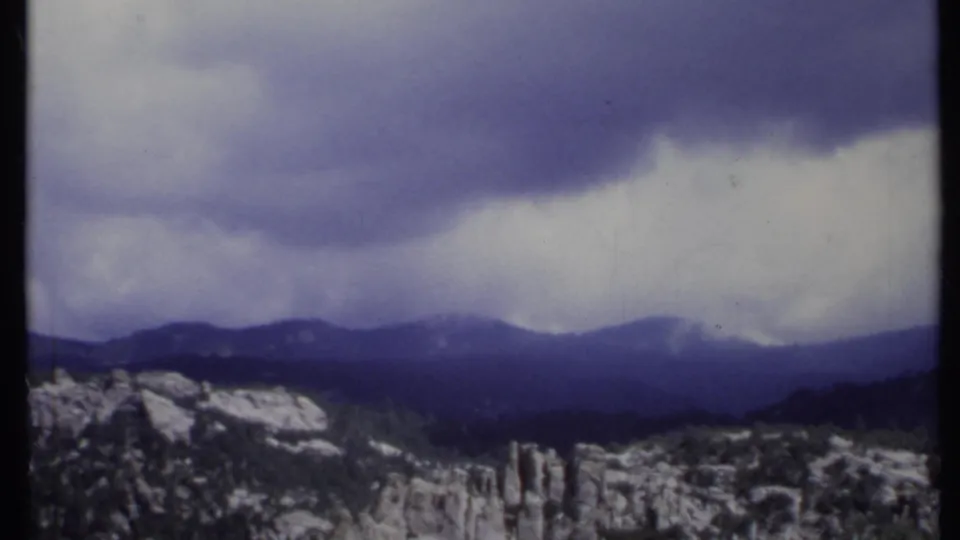 Soft 8mm frame of a California ridgeline and rocky foreground peaks beneath low, blue-gray cloud cover.