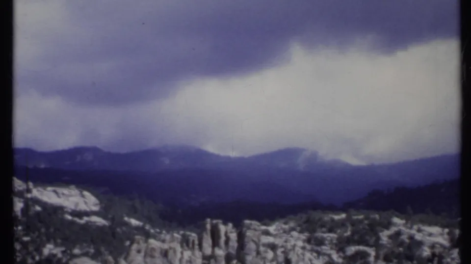 1971 8mm California landscape showing a cloud bank above dark mountains and snow-dusted rocky terrain.