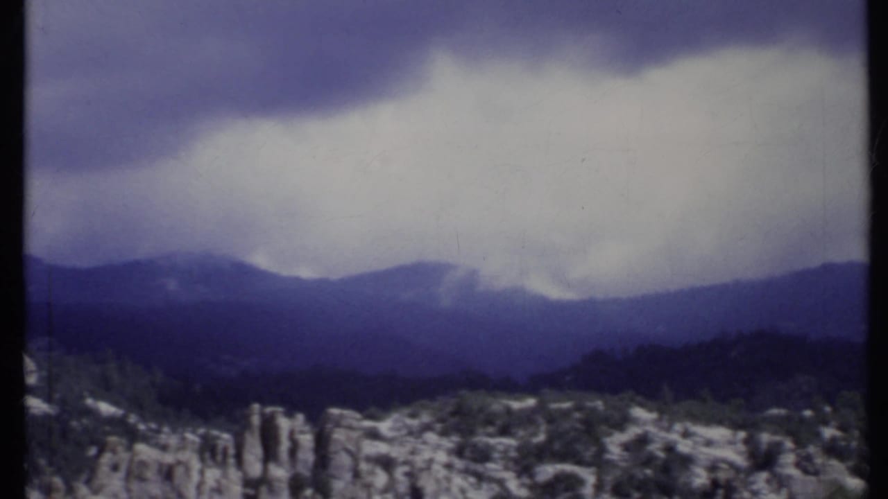 Cloudy mountain ridge above pale rocky outcrops and sparse shrubs.