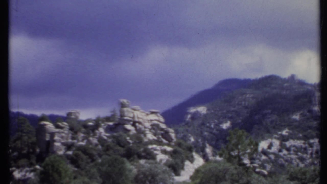 Rock formations and trees on a mountain hillside beneath a cloudy sky.