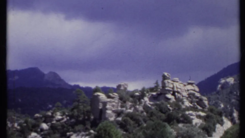 Soft 8mm frame of a California mountain landscape, with rocky terrain, trees, and distant ridges under low clouds.
