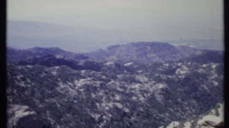 Vintage 8mm panorama of California mountain ridges, showing forested slopes, pale rock outcrops, and hazy distant hills.