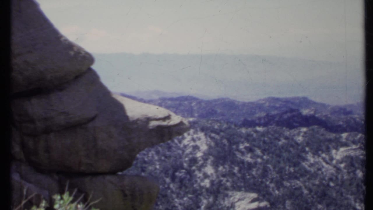 Rocky overlook with forested mountain ridges under a hazy sky.