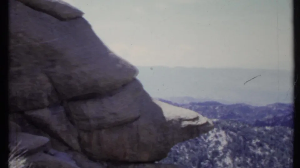 1971 California home-movie frame with a prominent rock outcrop at left and layered forested hills receding into haze.