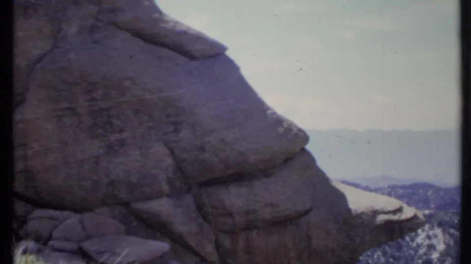 1971 California 8mm frame focusing on the textured rock outcrop, with hazy mountain terrain visible in the background.