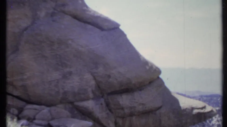 1971 California home-movie frame showing a broad rock face dominating the foreground as the mountain view continues behind it.