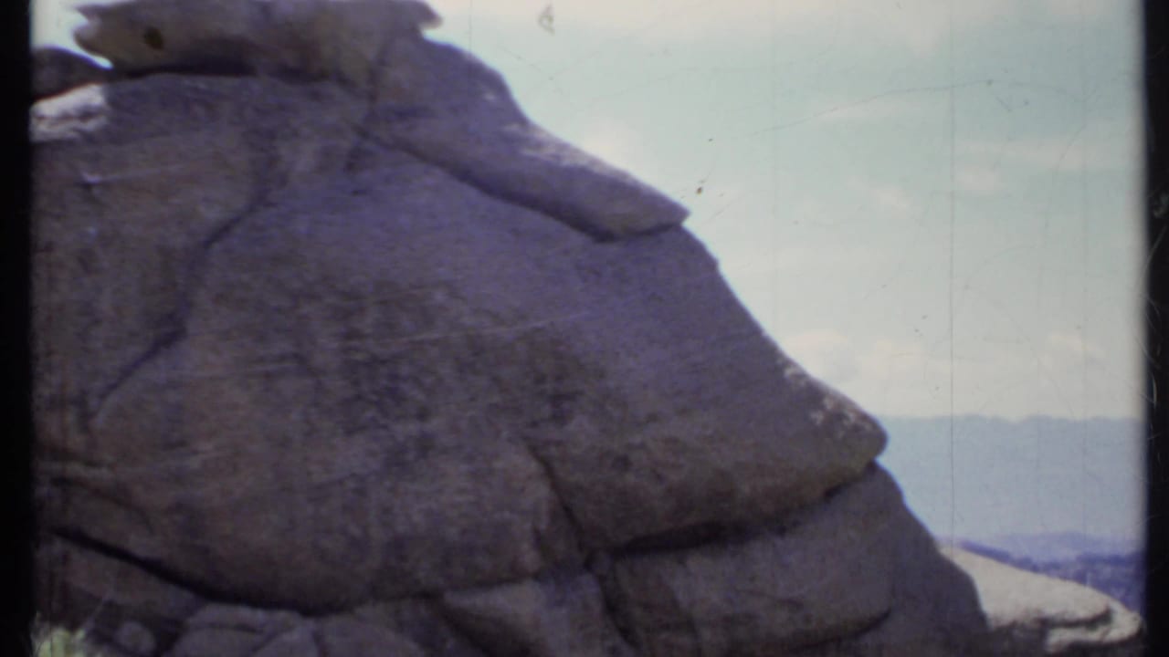 Close view of a large weathered boulder against pale sky and distant hills.