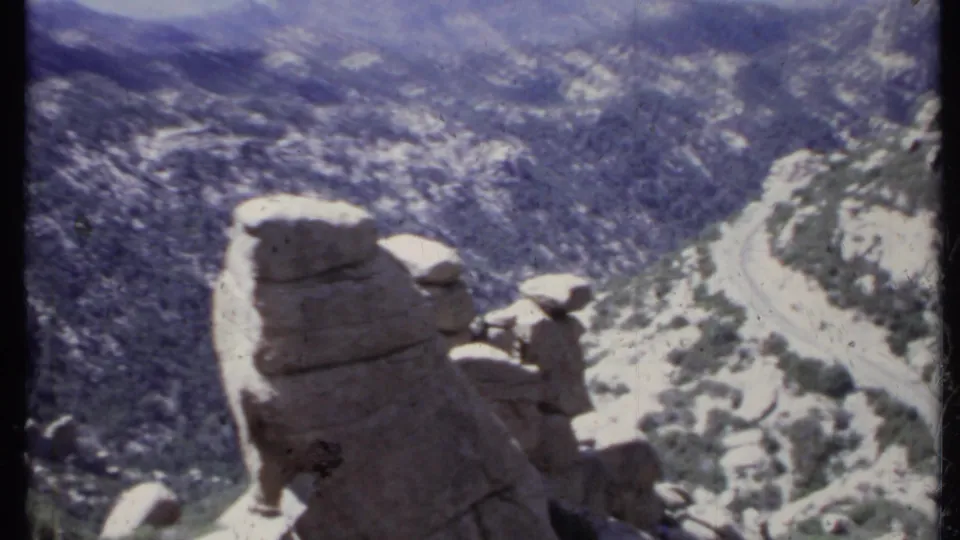 1971 California 8mm view of layered rock shapes, sparse brush, and a pale road cutting through arid hills.