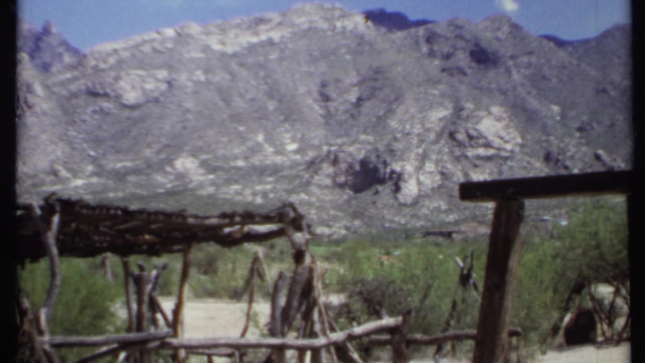 Rustic wooden shelter and fence below a rugged mountain range.