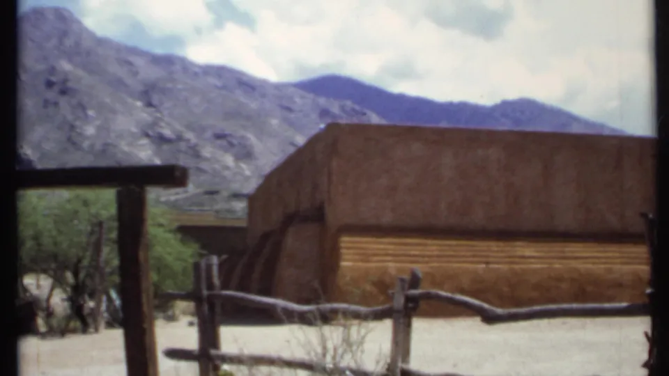 The pan ends on an adobe-style building and branch fence with California mountain terrain in the background.