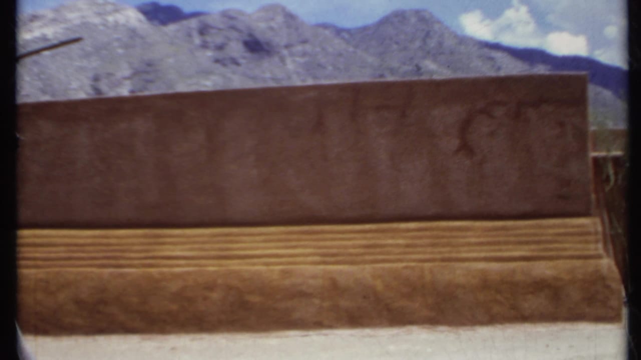 Adobe-style wall and stepped base with rocky mountains behind it.