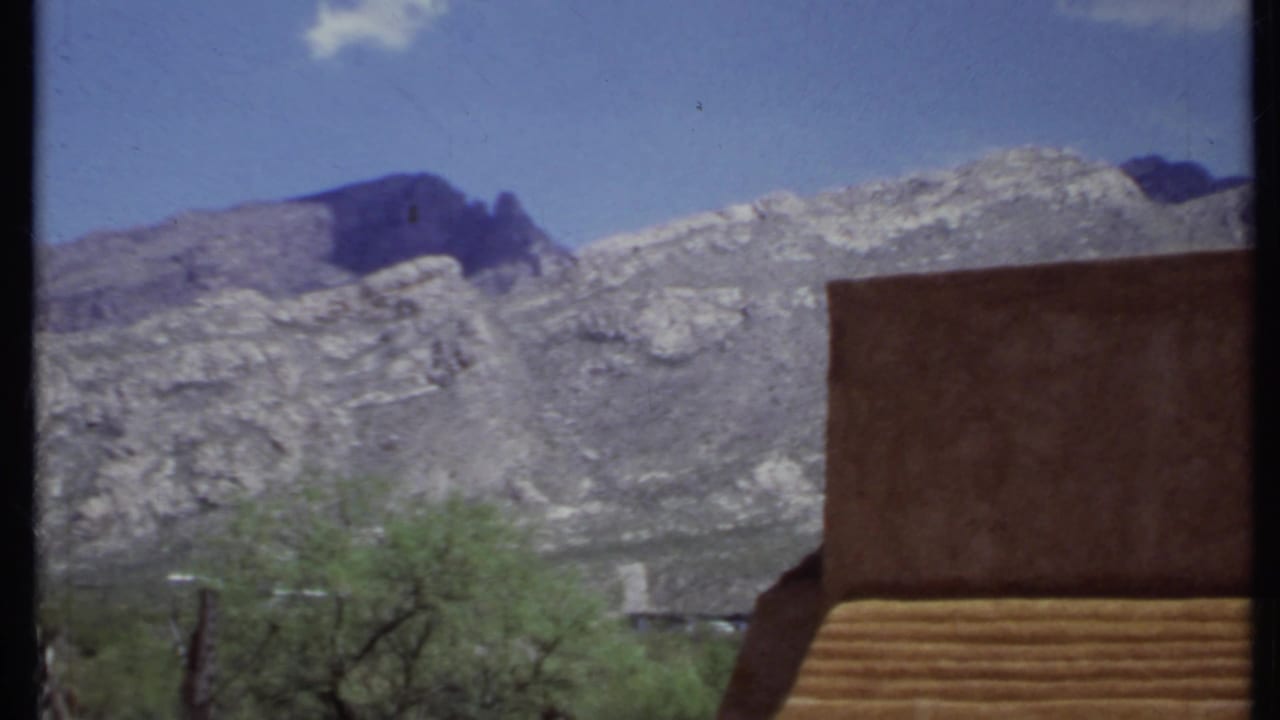 Rocky mountains behind an adobe-style wall and desert trees under a blue sky.