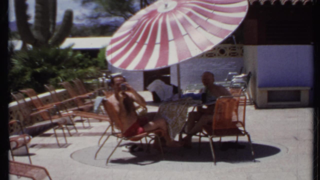 Two men sit at a patio table under a red-and-white striped umbrella.