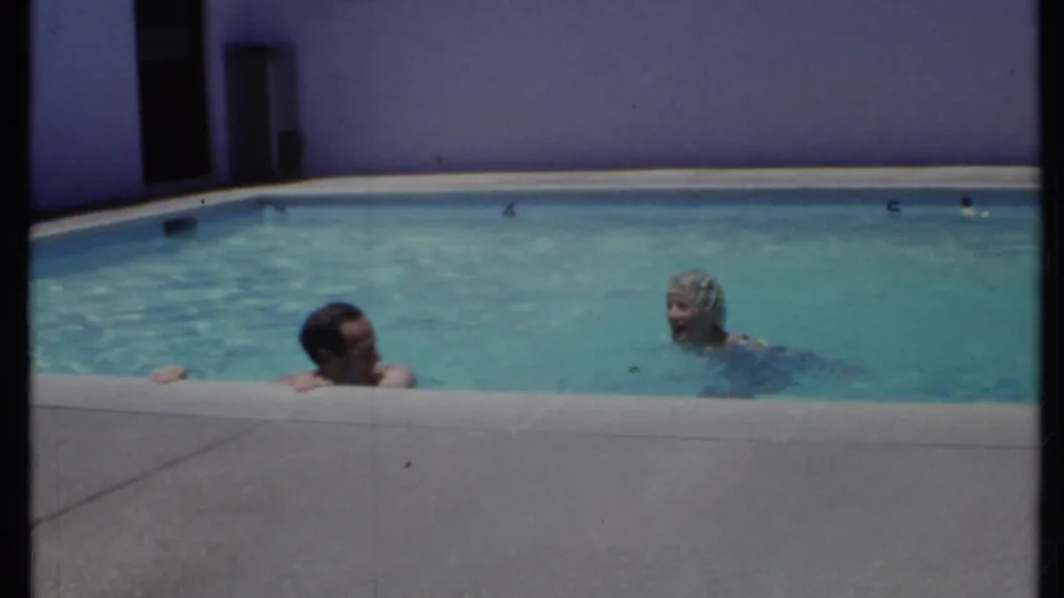 1971 California pool scene with two adult swimmers, including a woman in a swim cap, near a purple wall.